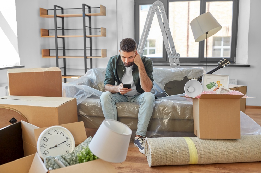 moving, eviction and real estate concept - sad man with smartphone and boxes at new home. sad man with smartphone and boxes moving home