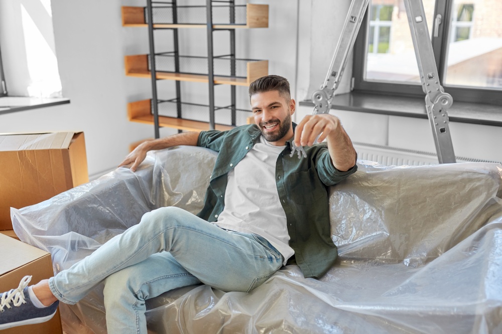 moving, people and real estate concept - happy smiling man with house keys and boxes at new home. man with house keys and boxes moving to new home