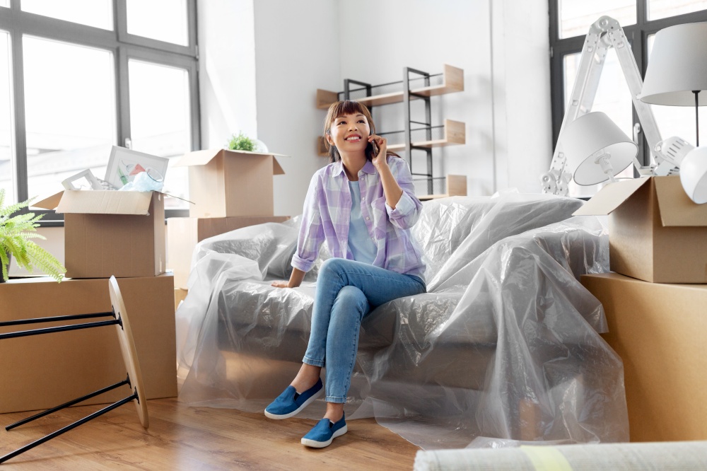 moving, people and real estate concept - happy smiling asian woman with boxes calling on smartphone at new home. happy woman calling on phone moving to new home