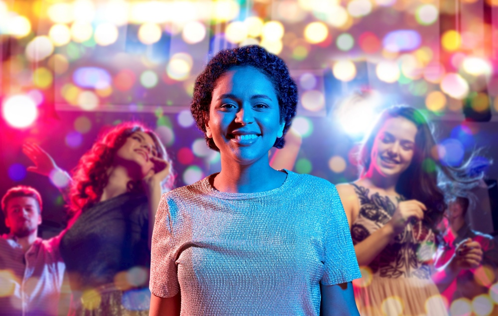 leisure, clubbing and nightlife concept - smiling young african american woman over ultraviolet neon lights over people dancin at nightclub background. african woman over neon lights at nightclub