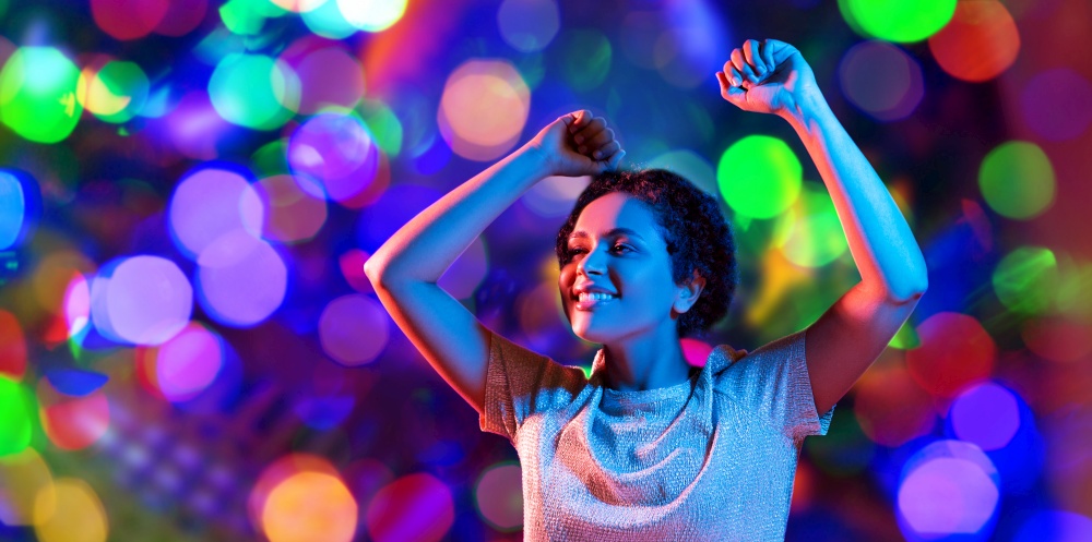 leisure, clubbing and nightlife concept - smiling young african american woman dancing in ultraviolet neon lights over bokeh background. african american woman dancing over neon lights