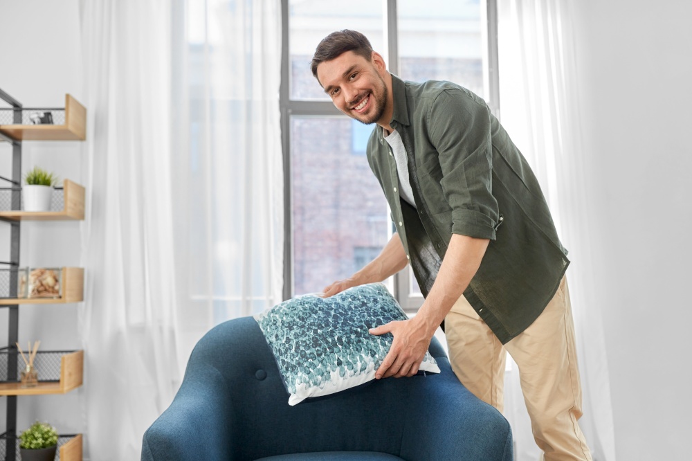 household, home improvement and cleaning concept - happy smiling man arranging cushion on armchair. happy smiling man arranging chair cushion at home