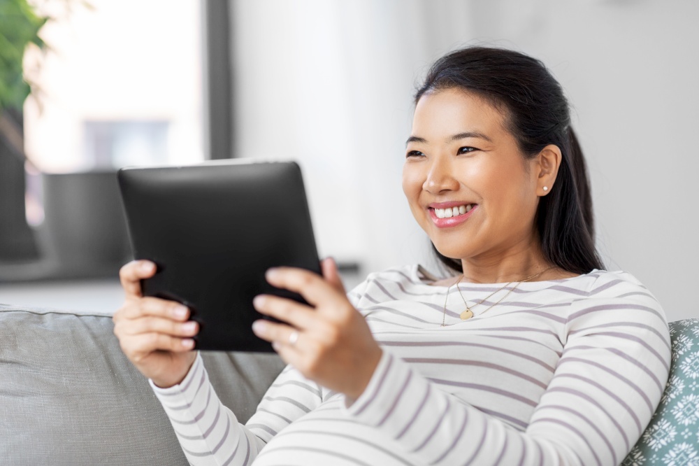 pregnancy, rest, people and expectation concept - happy smiling pregnant asian woman with tablet pc computer sitting on sofa at home. happy pregnant asian woman with tablet pc at home