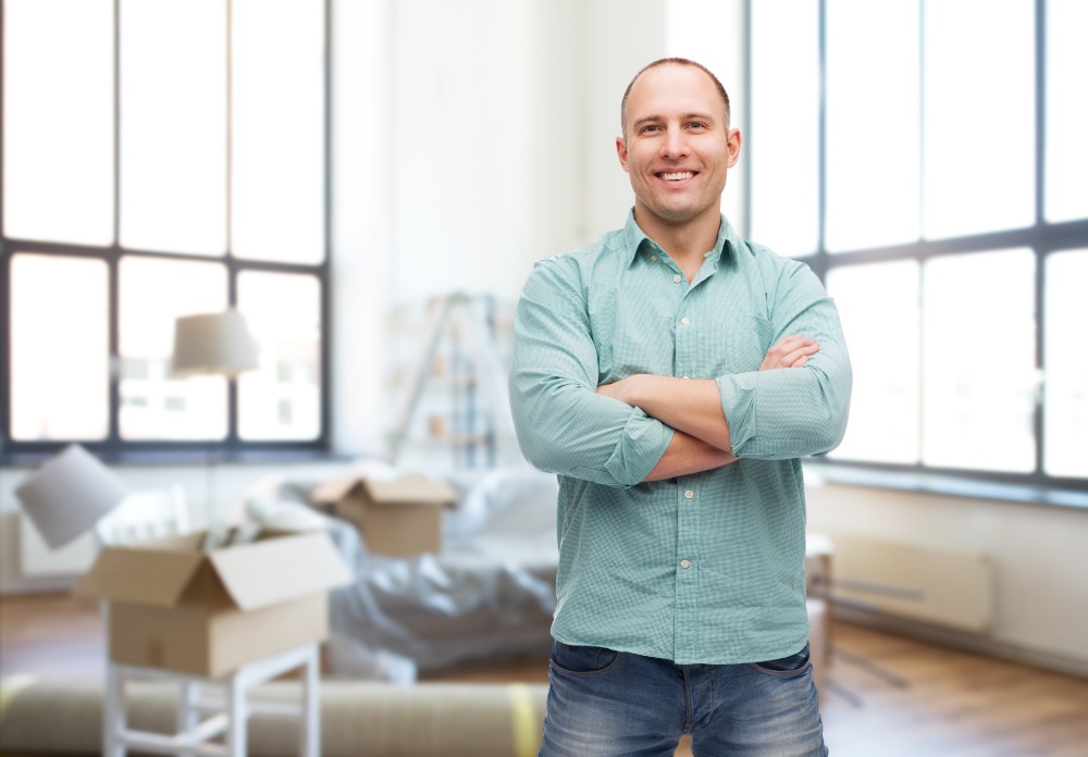 moving, real estate and people concept - smiling man with crossed arms over new home background. smiling man with crossed arms at new home