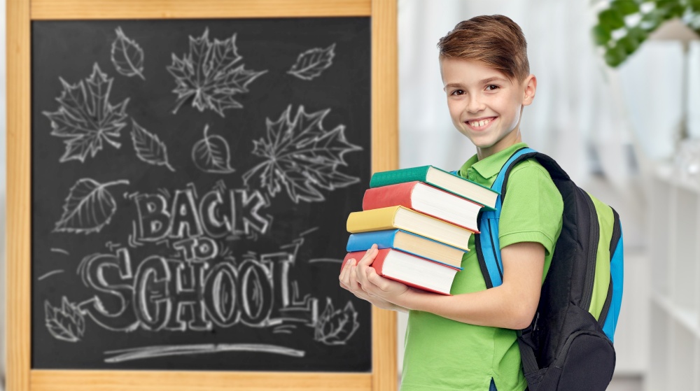 education, learning and people concept - happy smiling student boy with bag and books over chalkboard with back to school lettering on background. happy student boy with school bag and books