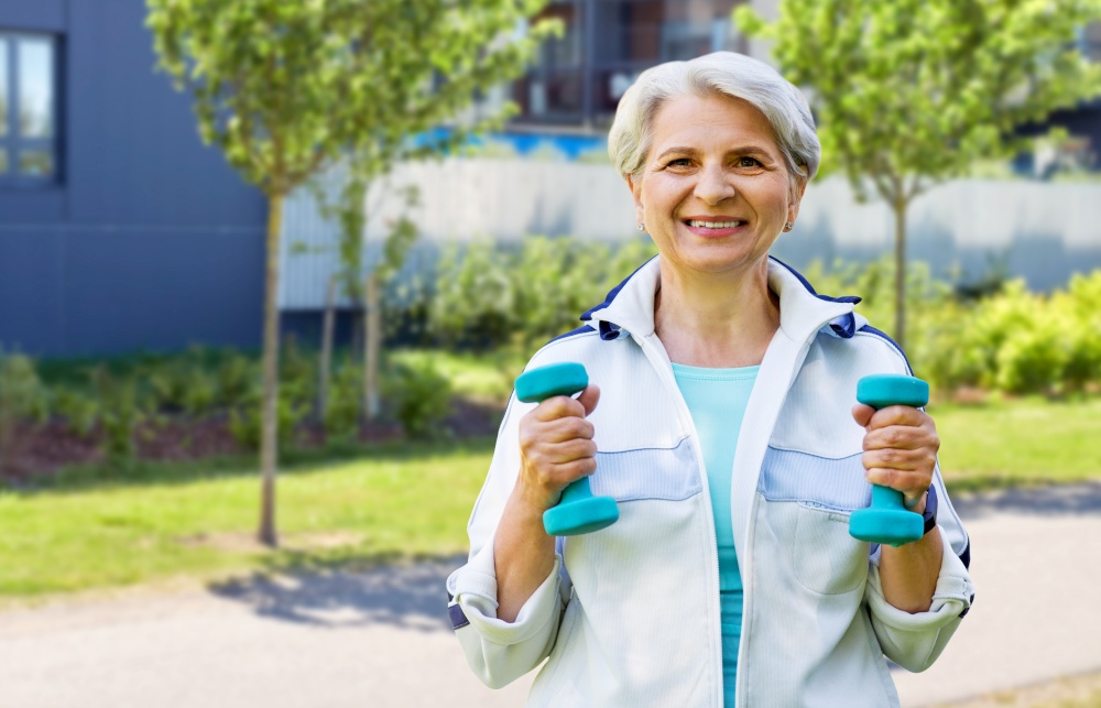 fitness, sport and healthy lifestyle concept - happy smiling senior woman with dumbbells exercising over city street background. senior woman with dumbbells exercising in city
