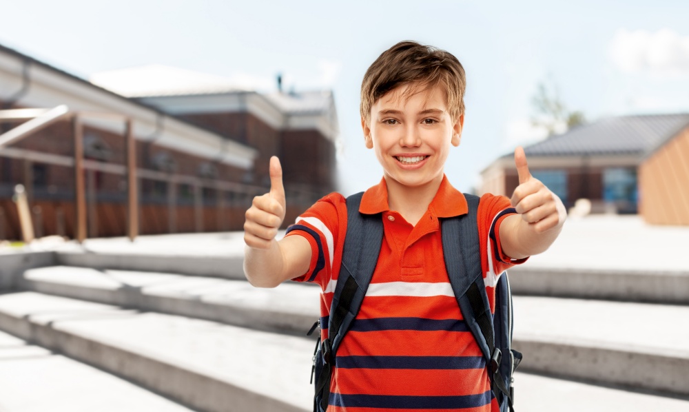 school, education and people concept - smiling student boy with backpack showing thumbs up over city street background. happy student boy with backpack showing thumbs up