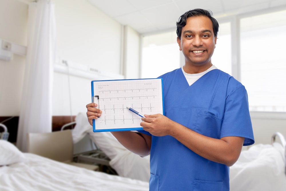healthcare, cardiology and medicine concept - happy smiling indian doctor or male nurse in blue uniform with cardiogram on clipboard over hospital ward background. smiling male doctor with cardiogram on clipboard