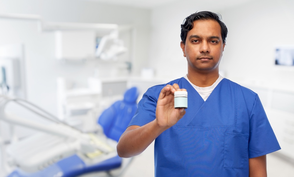 medicine, stomatology and healthcare concept - indian doctor or male dentist holding jar of pills over dental clinic office background. indian doctor holding medicine at dental office