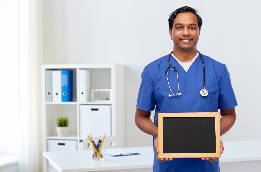 healthcare, profession and medicine concept - happy smiling indian male doctor or nurse in blue uniform with chalkboard and stethoscope over medical office at hospital background. happy indian male doctor or nurse with chalkboard