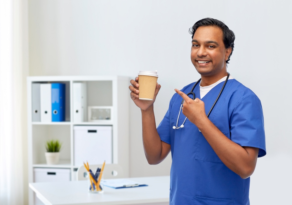 healthcare, profession and medicine concept - happy smiling indian doctor or male nurse in blue uniform with takeaway coffee cup and stethoscope over medical office at hospital background. male doctor with stethoscope drinking coffee