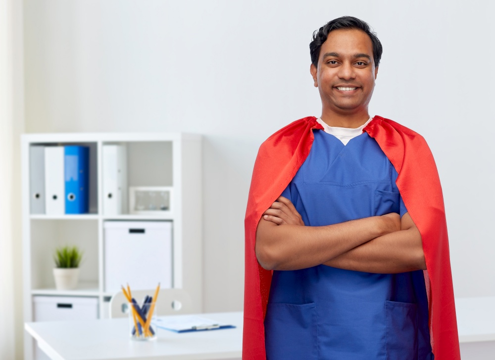 healthcare, profession and medicine concept - happy smiling indian doctor or male nurse in blue uniform and red superhero cape over medical office at hospital background. smiling doctor or male nurse in superhero cape