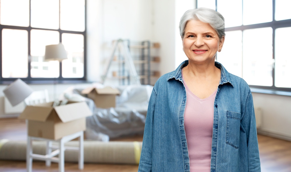 moving, real estate and people concept - smiling senior woman in denim shirt over new home background. portrait of smiling senior woman at new home