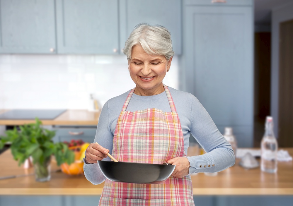 food cooking, culinary and old people concept - portrait of smiling senior woman in apron with frying pan over kitchen background. smiling senior woman in apron with frying pan
