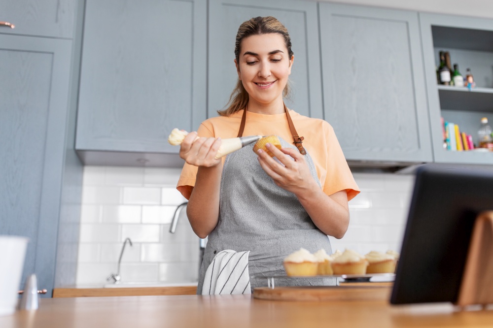 culinary, bake and cooking food concept - happy smiling young woman with baking bag making cupcake topping on kitchen at home. woman cooking food and baking on kitchen at home