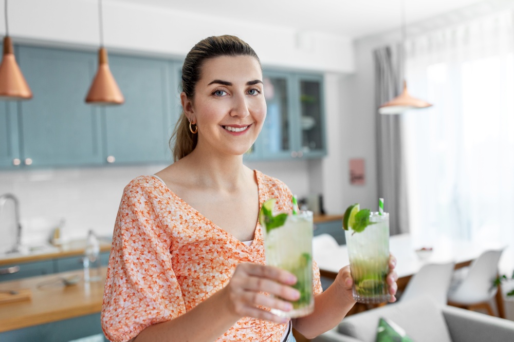 culinary, drinks and people concept - happy smiling young woman holding glass of lime mojito cocktails at home kitchen. woman with lime mojito cocktail at home kitchen