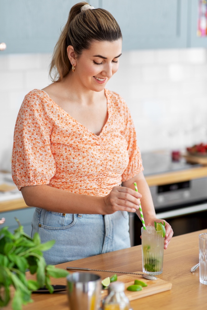 culinary and people concept - happy smiling young woman making cocktail drinks with lime and peppermint at home kitchen. woman making cocktail drinks at home kitchen
