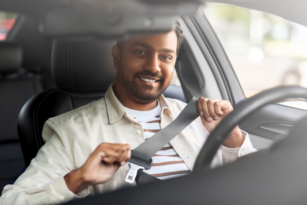 transport, safety and people concept - happy smiling indian man or driver fastening seat belt in car. smiling indian man or driver driving car