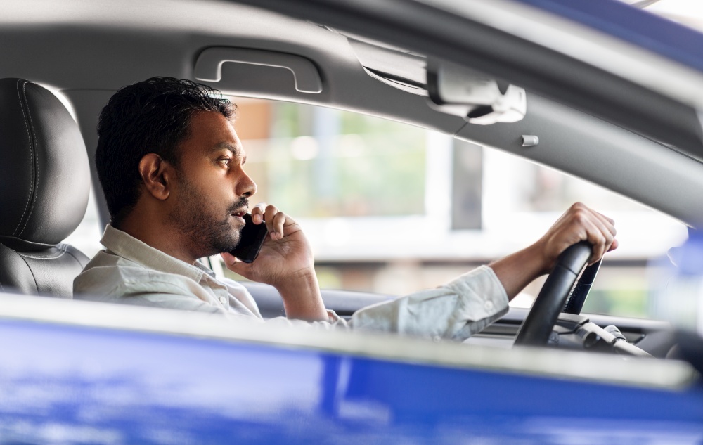 transport, communication and people concept - indian man or driver driving car and calling on smartphone. indian man driving car and calling on smartphone