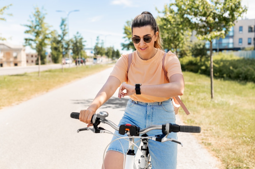 people, leisure and lifestyle - happy smiling young woman with smart watch riding bicycle on city street. woman with smart watch riding bicycle in city