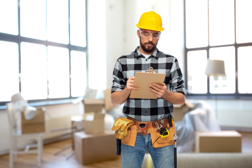 repair, construction and building concept - male worker or builder in helmet with clipboard over home room background. male builder in helmet with clipboard at home