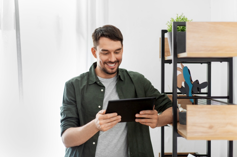 home improvement and decoration and people concept - happy smiling man with tablet pc computer standing at shelf at home. happy smiling man with tablet pc at shelf at home