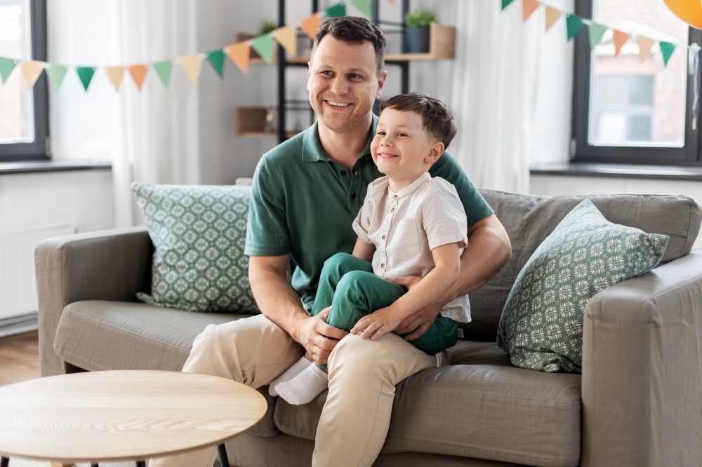 family, fatherhood and people concept - portrait of happy smiling father and little son sitting on sofa at home party. happy father and little son at home birthday party