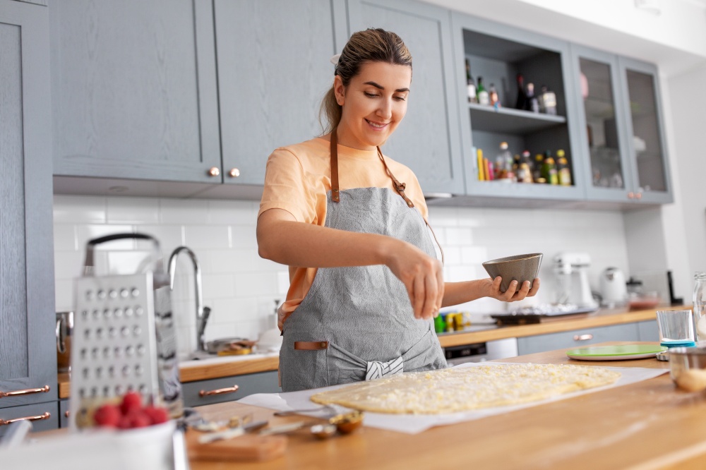 culinary, cooking food and people concept - happy smiling young woman with dough baking pie on kitchen at home. woman cooking food and baking on kitchen at home
