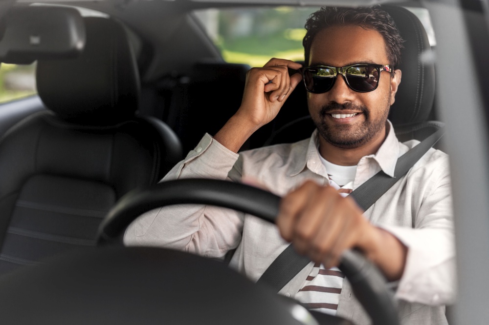 transport, vehicle and people concept - happy smiling indian man or driver in sunglasses driving car. smiling indian man in sunglasses driving car