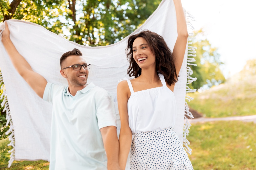 leisure, vacation and people concept - happy couple with picnic blanket walking at summer park. happy couple with picnic blanket at summer park