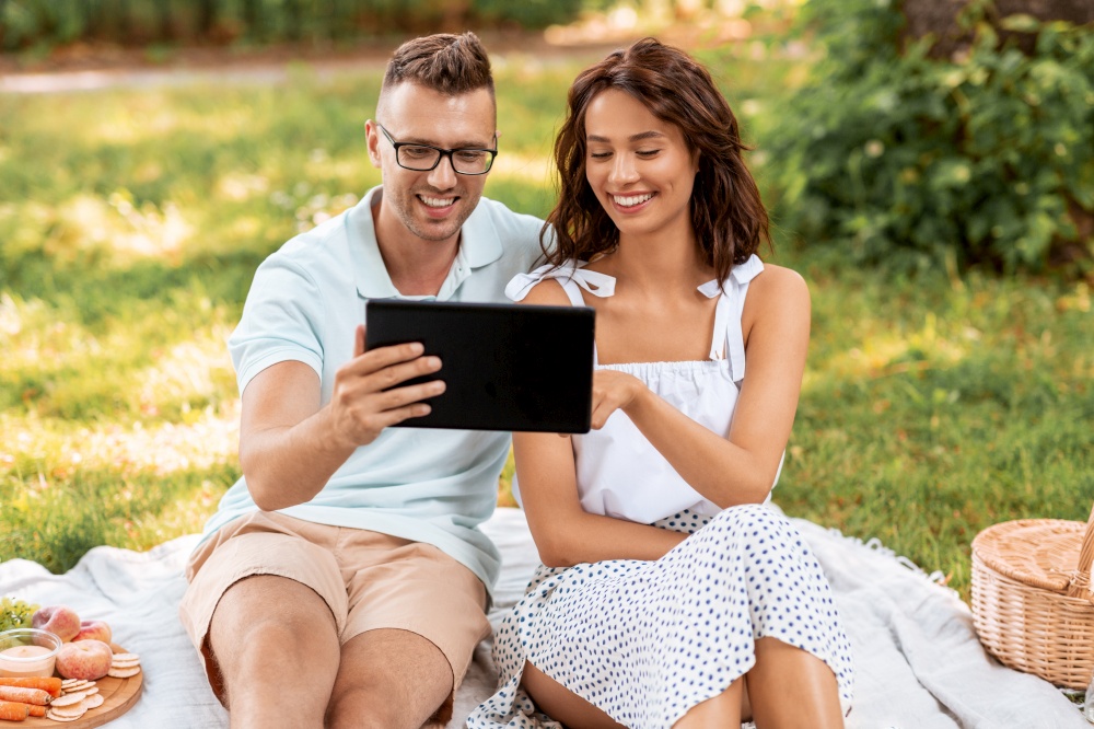 leisure and people concept - happy couple with tablet pc computer having picnic at summer park. happy couple with tablet pc at picnic in park
