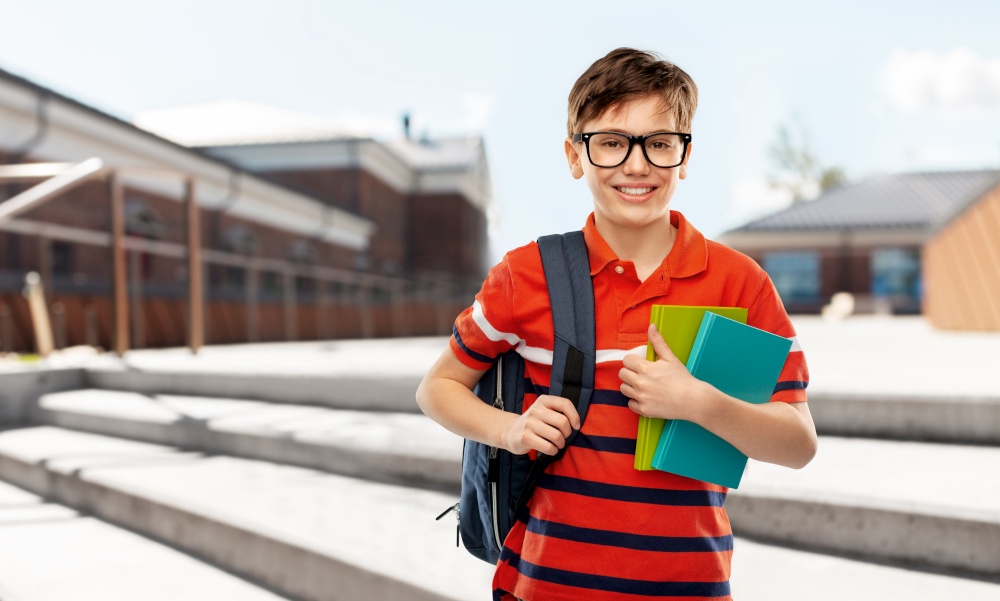 school, education and people concept - smiling student boy in glasses with backpack and books over city street background. smiling student boy with backpack and books