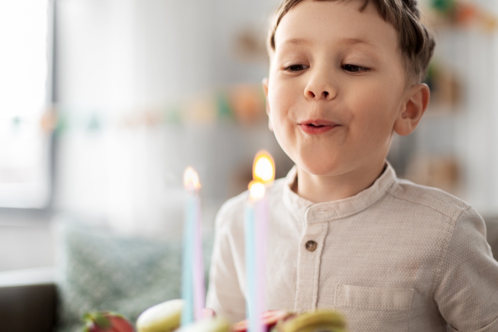 holidays, celebration and people concept - happy little boy blowing candles on birthday cake at home party. happy little boy blowing candles on birthday cake