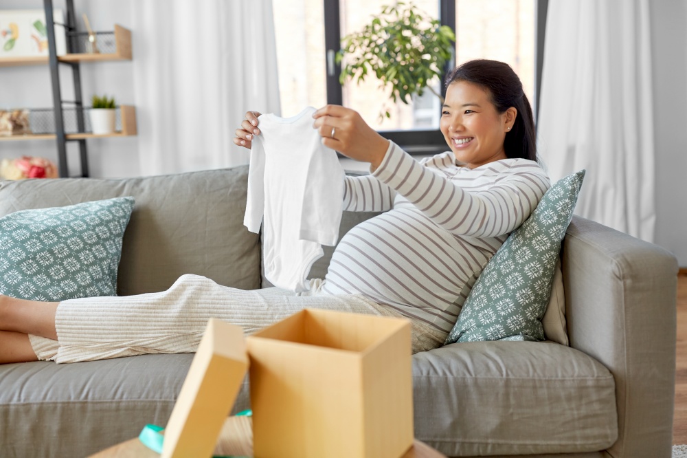 pregnancy, holidays and people concept - happy smiling pregnant asian woman opening gift box with baby&rsquo;s bodysuit at home. happy pregnant woman with baby&rsquo;s bodysuit at home