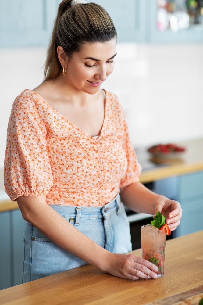 culinary, drinks and people concept - happy smiling young woman making strawberry mojito cocktail at home kitchen. woman making cocktail drinks at home kitchen