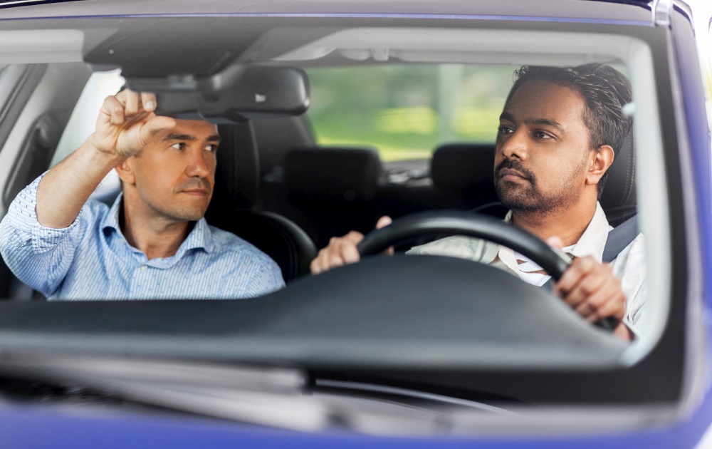 driver courses and people concept - man and driving school instructor adjusting mirror in car. car driving school instructor teaching male driver