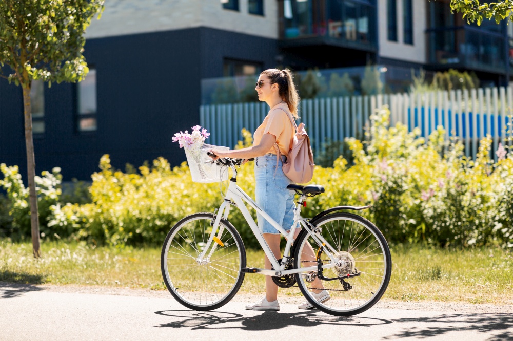 people, leisure and lifestyle - happy young woman with flowers in basket of bicycle and backpack walking on city street. woman with flowers in bicycle basket in city