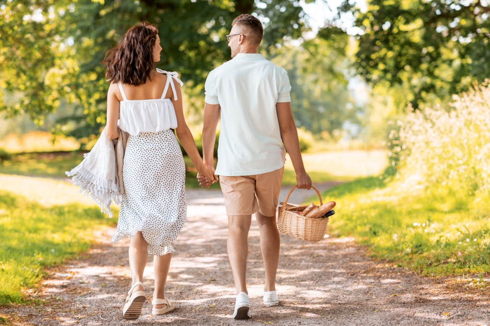 leisure, vacation and people concept - happy couple with picnic basket and blanket walking at summer park. happy couple with picnic basket at summer park