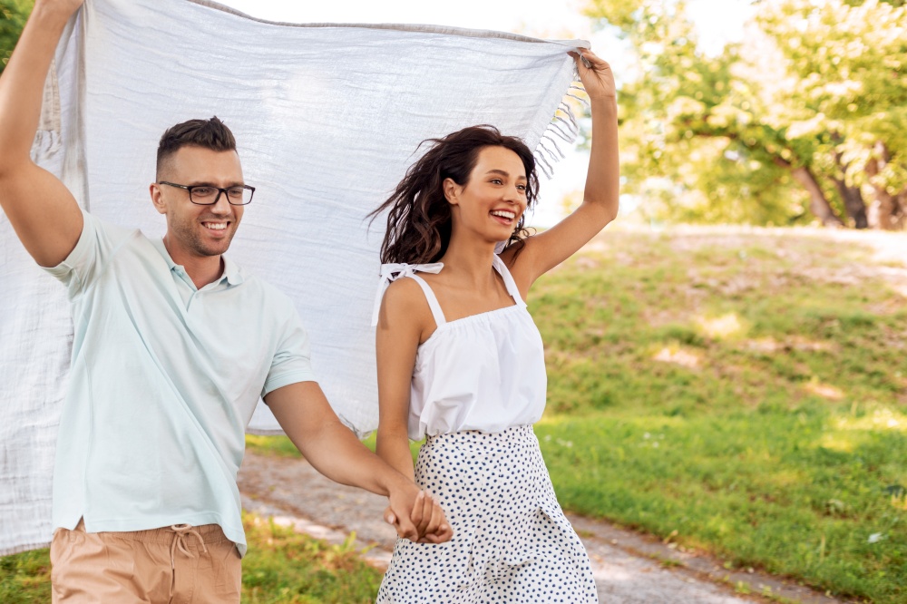 leisure, vacation and people concept - happy couple with picnic blanket walking at summer park. happy couple with picnic blanket at summer park