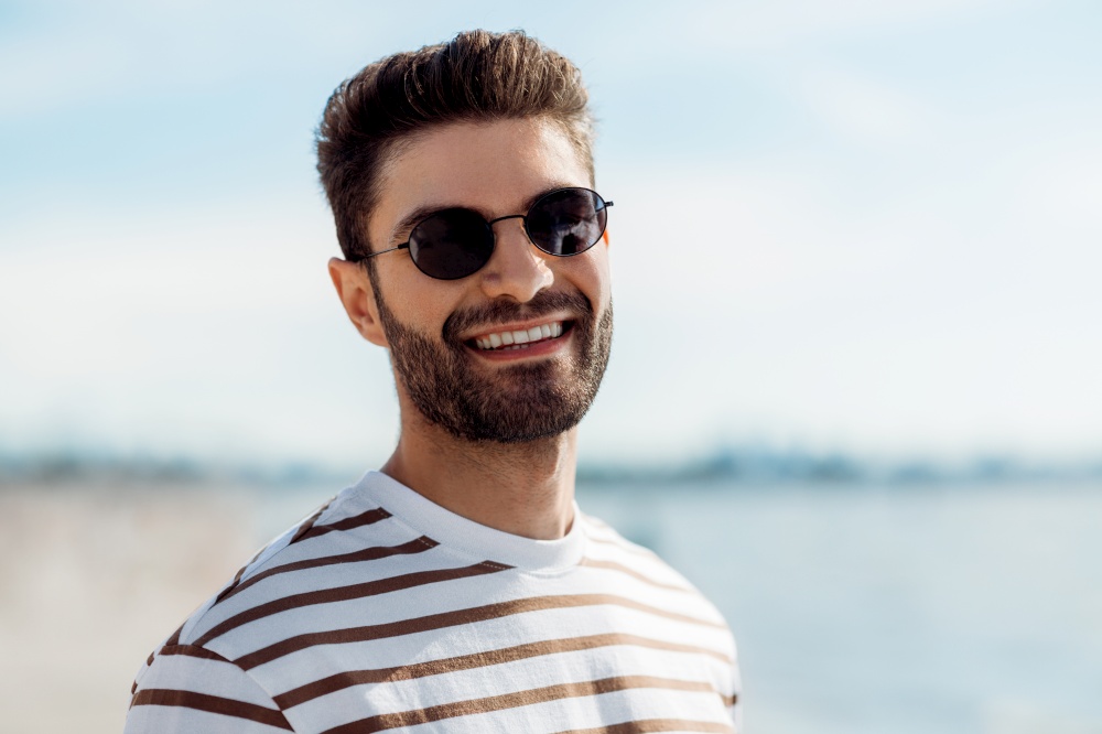 summer holidays and people concept - portrait of happy smiling young man in sunglasses on beach. smiling young man in sunglasses on summer beach