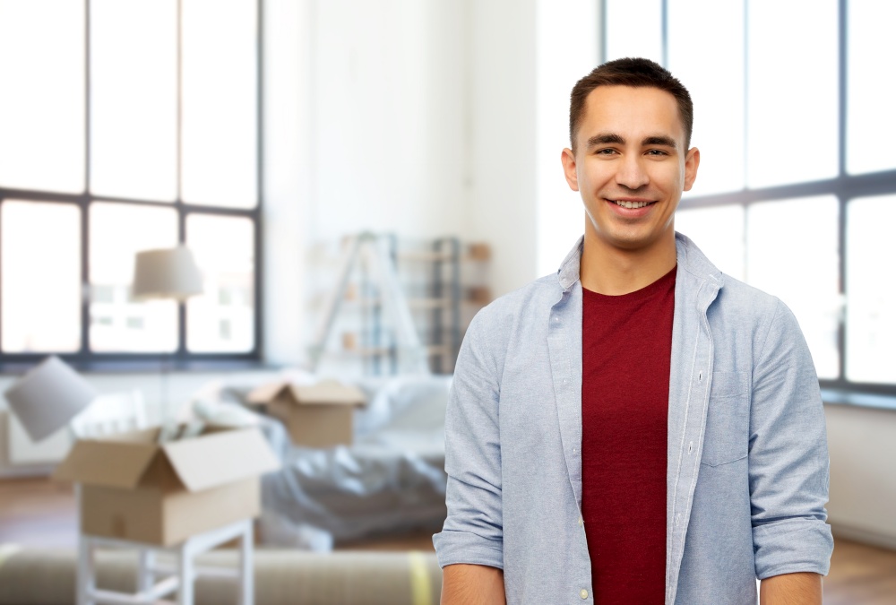 moving, real estate and people concept - smiling young man over new home background. smiling young man over new home background