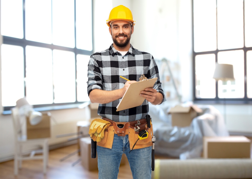 repair, construction and building concept - happy smiling male worker or builder in helmet with clipboard over home room background. male builder in helmet with clipboard at home