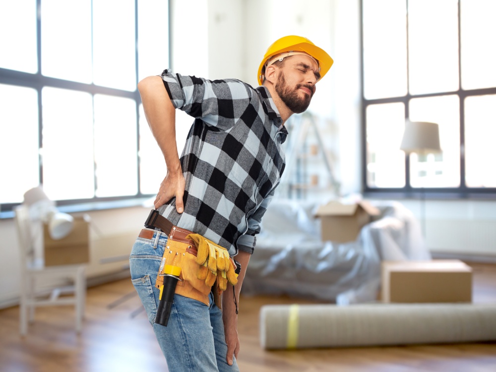 repair, construction and building concept - male worker or builder in helmet having back ache over home room background. male worker or builder having back ache at home
