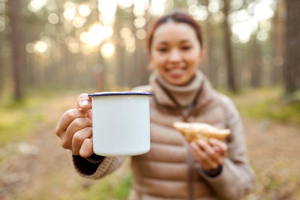 picking season, leisure and people concept - close up of young asian woman with mug drinking tea in autumn forest. asian woman with mug drinking tea in forest