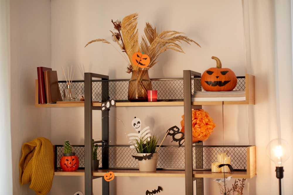 holidays, celebration and party concept - jack-o-lantern or carved pumpkin and other halloween decorations on shelf at home. shelf with halloween decorations at home