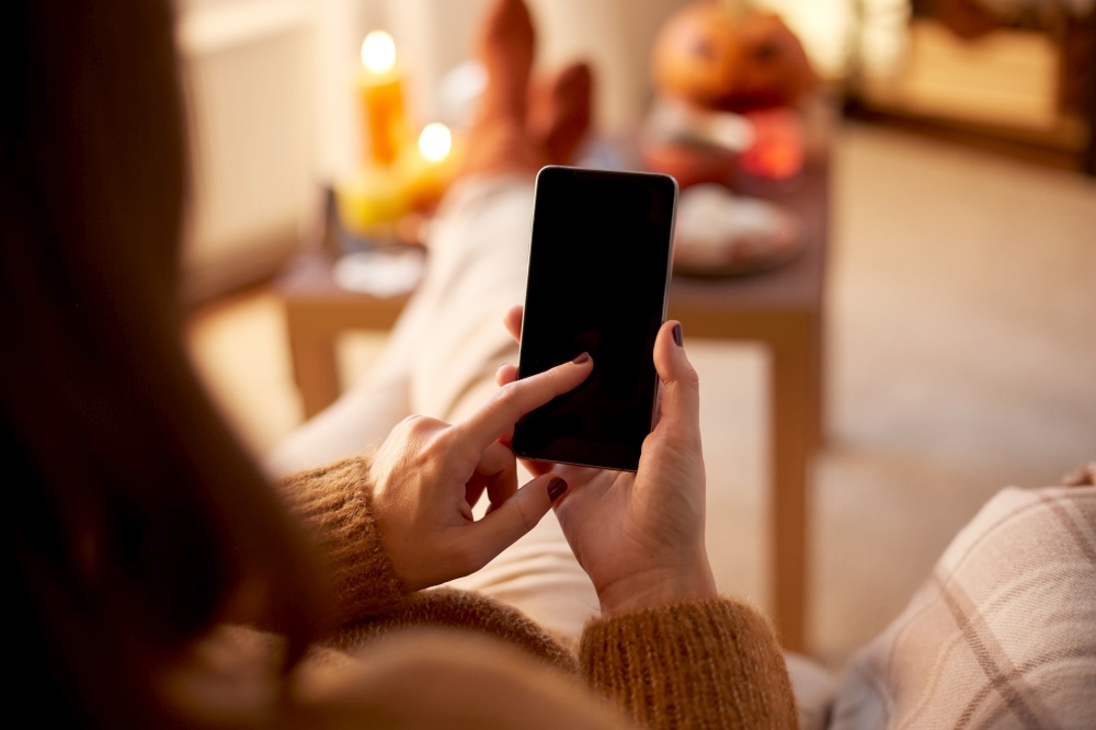 halloween, holidays and leisure concept - close up of young woman using smartphone at home. woman using smartphone at home on halloween