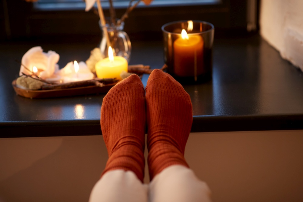 halloween, hygge and leisure concept - close up of feet in socks on window sill at home in autumn. feet in socks on window sill at home in autumn
