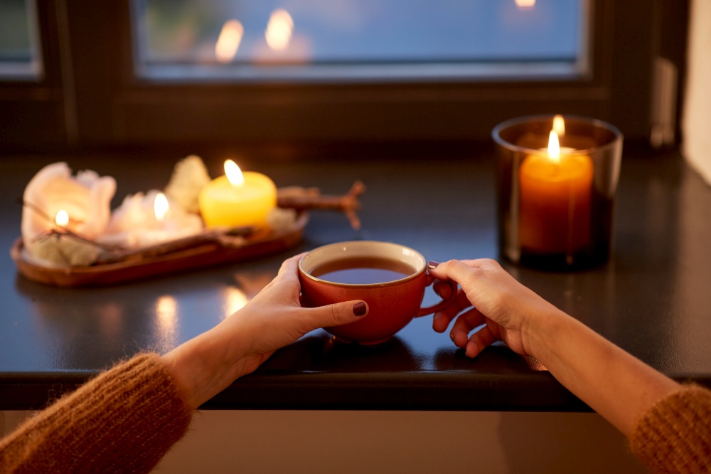 drinks, seasons and leisure concept - woman&rsquo;s hands with cup of tea on window sill in autumn. hands with cup of tea on window sill in autumn