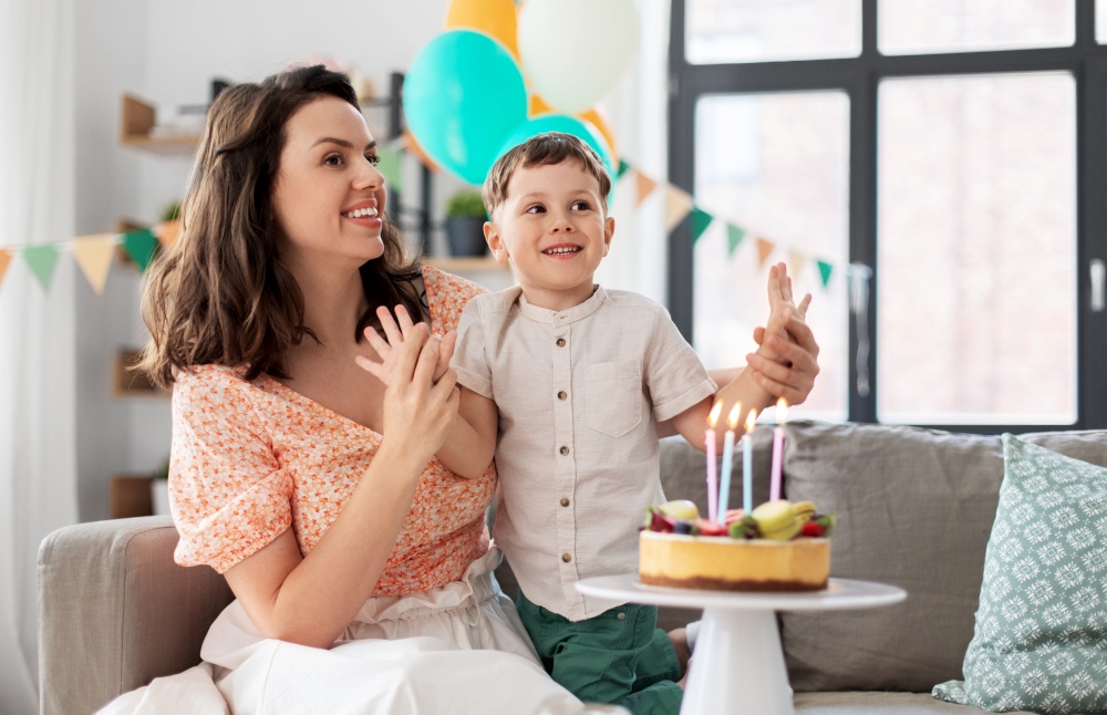 family, holidays and people concept - portrait of happy smiling mother and little son with birthday cake at home party. happy mother and son with birthday cake at home
