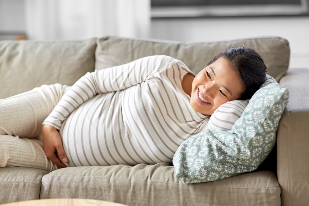 pregnancy, rest, people and expectation concept - happy smiling pregnant asian woman lying on sofa at home. happy pregnant asian woman lying on sofa at home